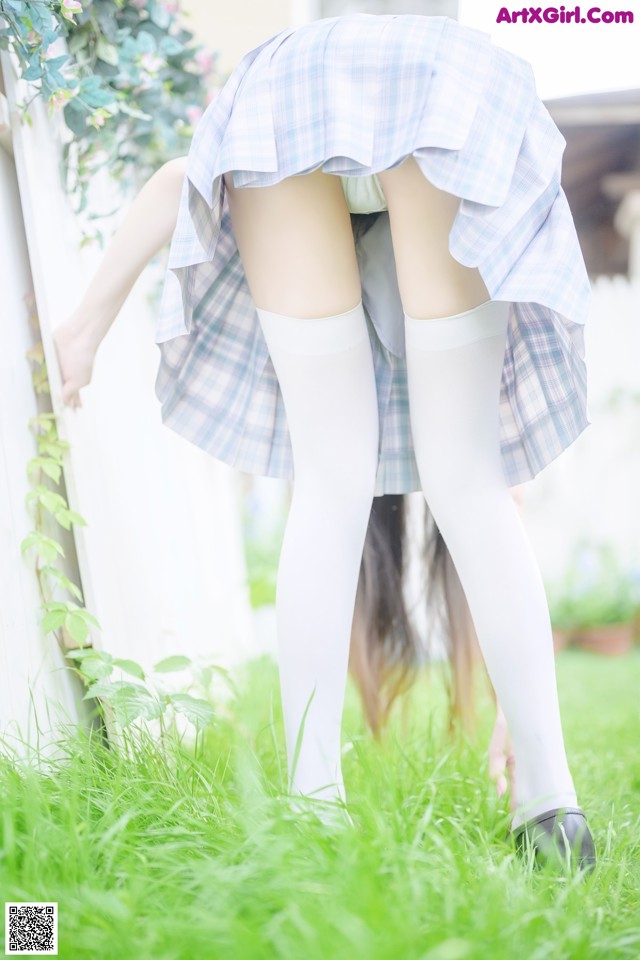 A woman in a plaid skirt and white stockings bending over in the grass.