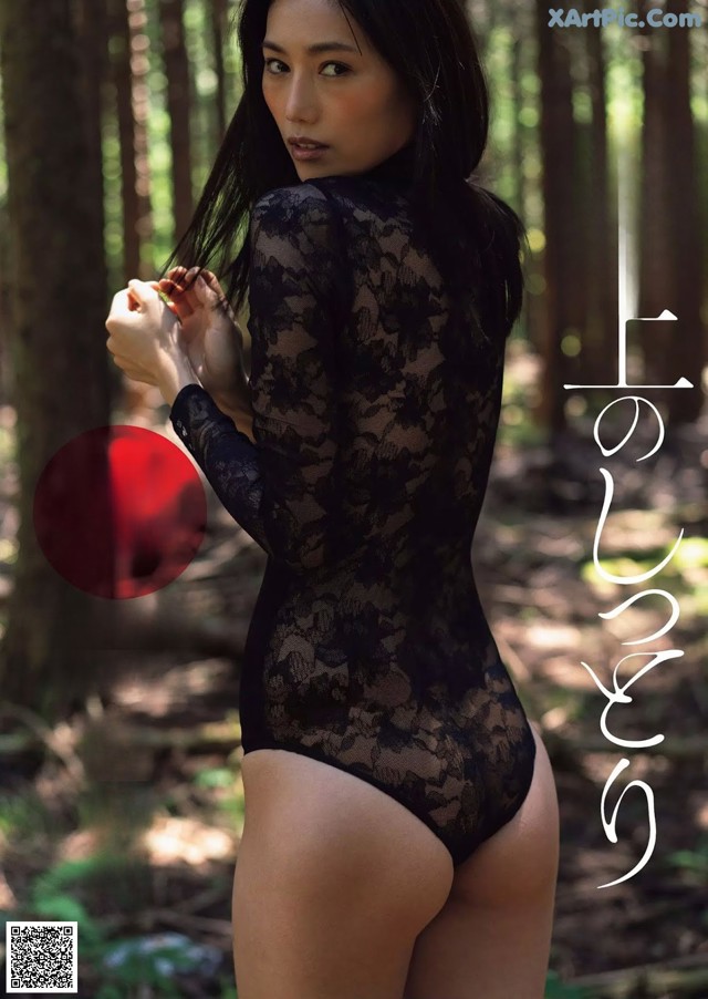 A woman in a black bodysuit standing in the woods.