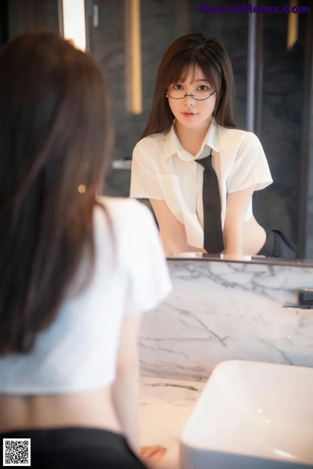 A woman in a white shirt and black tie looking at herself in the mirror.