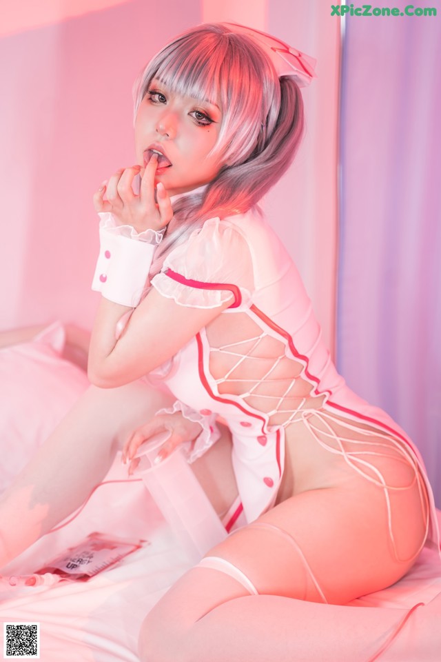 A woman in a pink and white outfit sitting on a bed.