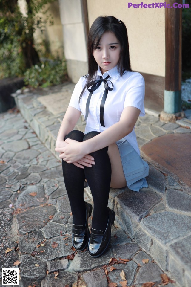 A woman in a school uniform sitting on a stone ledge.