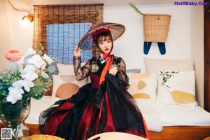 A woman in a kimono sitting on a bed with an umbrella.