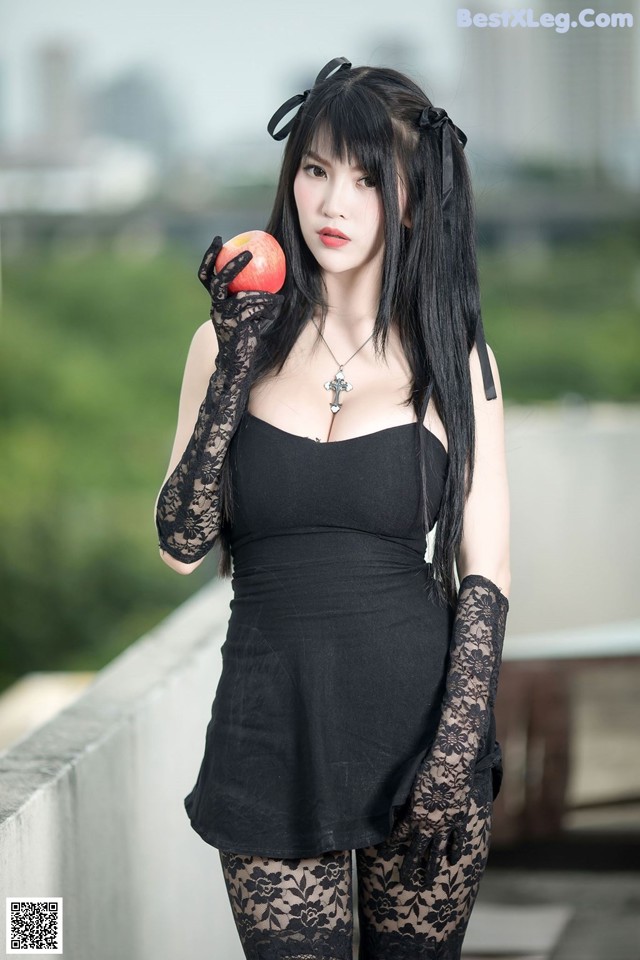 A woman in a black dress holding an apple.