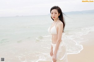 A woman in a white bikini sitting on the beach.