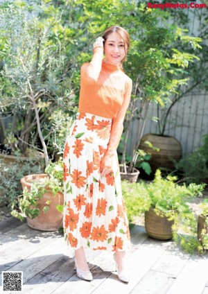 A woman in an orange shirt is standing in front of a book.