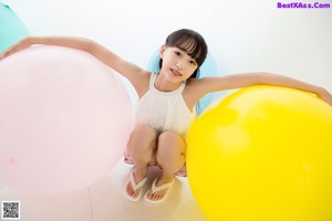 A young girl sitting on a pink rug next to balloons.