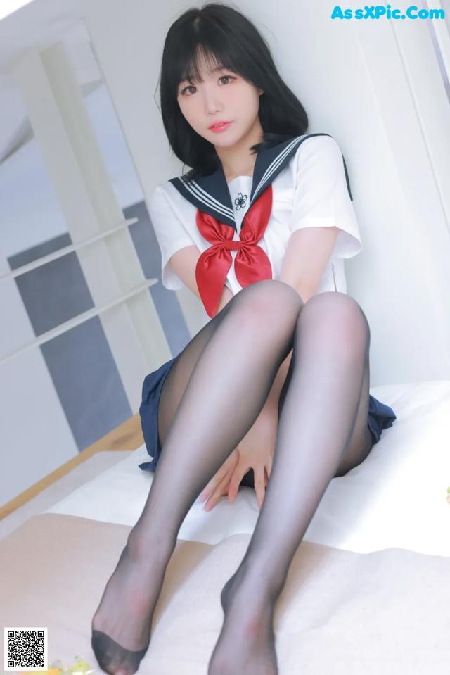 A woman in a sailor outfit sitting on a bed.