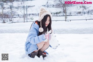 A woman sitting in the snow wearing a blue jacket and boots.