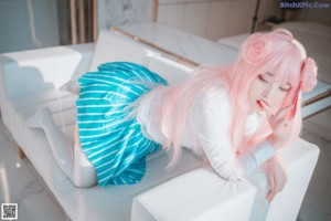 A woman with pink hair sitting on a bed.