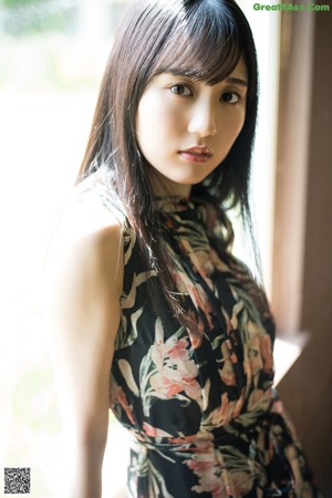 A woman with long black hair standing in front of a window.