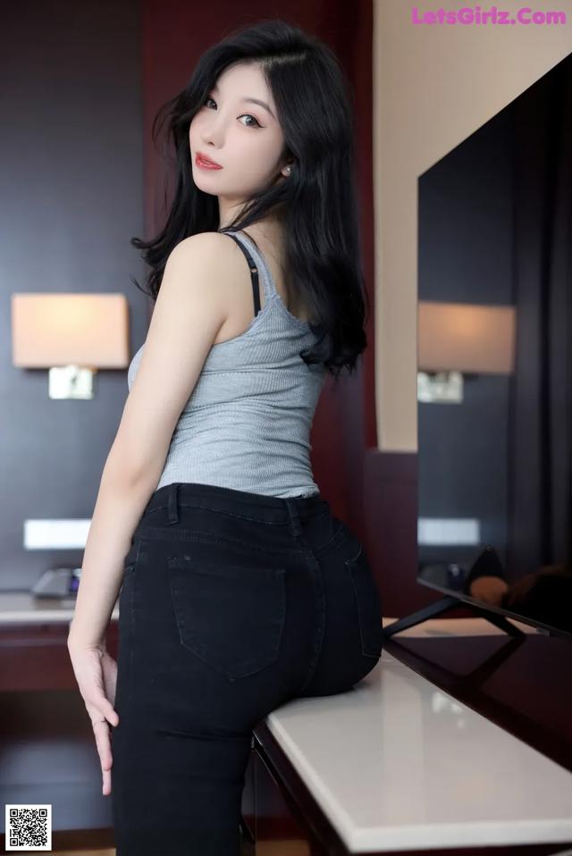 A woman in a gray tank top and black jeans posing for a picture.