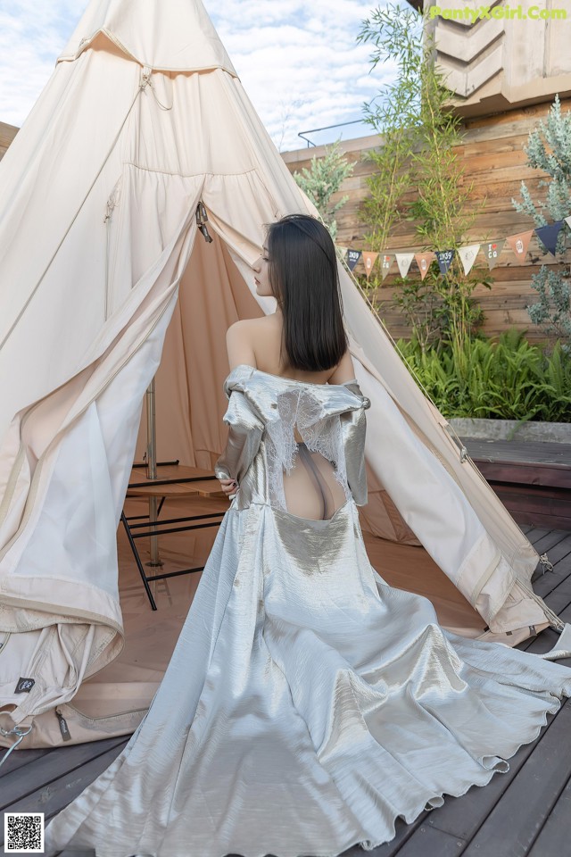 A woman in a wedding dress standing in front of a teepee.