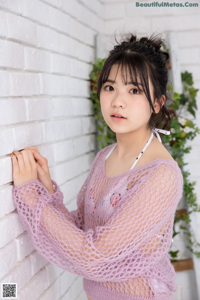 A woman in a pink sweater leaning against a white brick wall.