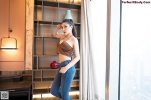 A woman in a brown top and blue jeans posing for a picture.