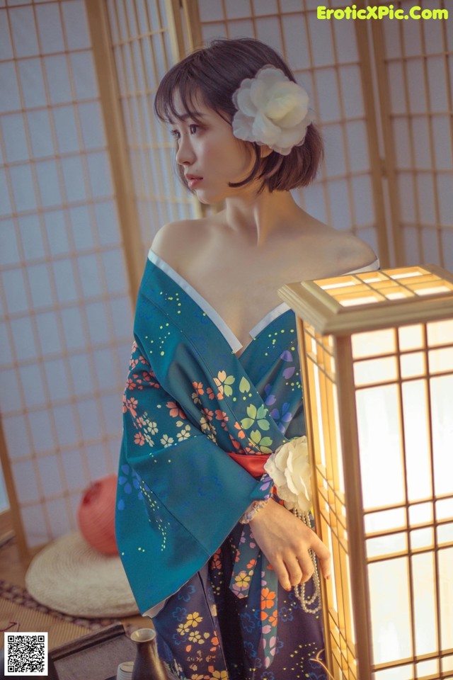 A woman in a blue kimono standing next to a lamp.