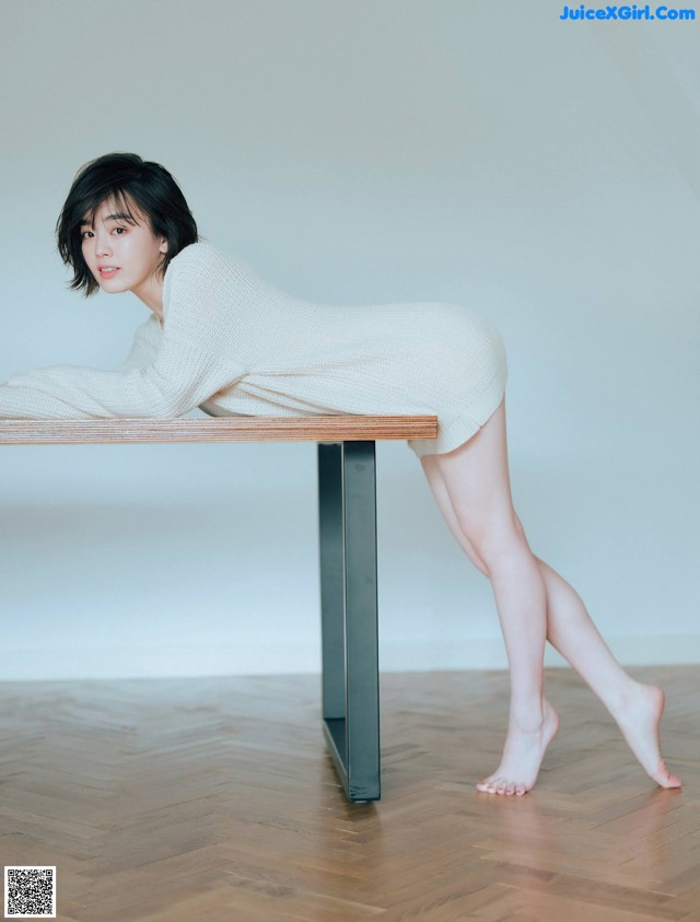 A woman leaning on a wooden table with her legs crossed.