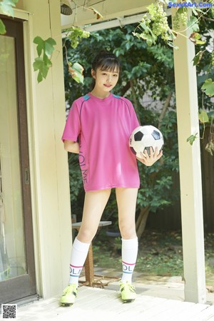 A young girl in a pink shirt kicking a soccer ball.