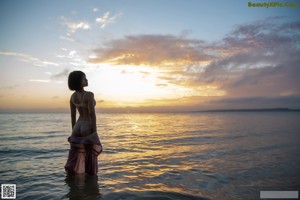 A woman in a pink dress is standing in the water.