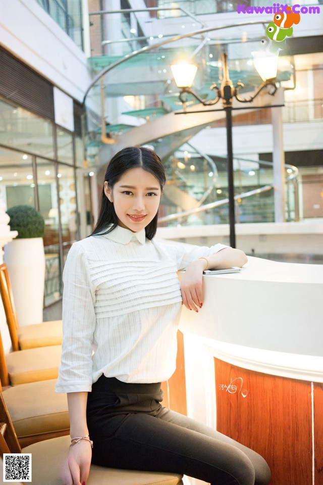 A woman sitting on a chair in a white shirt and black pants.