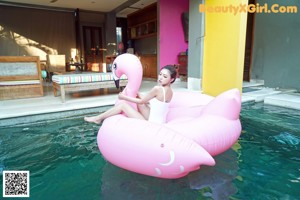 A woman in a white bathing suit sitting on a lounge chair next to a pool.
